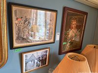 Three framed prints hanging on a blue wall, showing a courtroom scene, a woman portrait, and a street scene with umbrellas.
