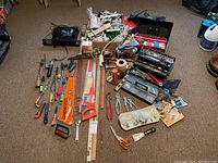 Overview of household tools including hand saws, pliers, screwdrivers, measuring yardsticks, scissors, paint tools, and open tool chests with miscellaneous items