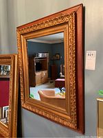 Front view of rectangular mirror showing wood and composite frame with carved floral patterns, mounted on wall reflecting room interior.