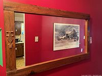 Full view of wall mirror with wood frame and carved detail on left side, reflecting room