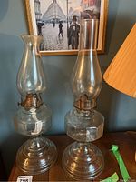 Two glass oil lamps standing side by side on a surface, showing their matching bases and different glass shades and wick holders.