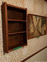 View of wooden shelf and framed painting hanging on wallpapered wall.