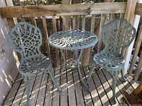 Set of cast aluminum outdoor patio table and two chairs on wooden deck, showing overall look and condition.