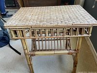 Side view of rattan side table showing woven top, frame details and magazine shelf below