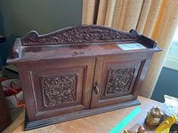 Front view of the vintage wooden tabletop cabinet showing detailed carved floral and dragon panels on two doors and decorative top back rail.