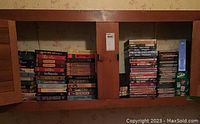 Shelf with stacked VHS tapes and DVDs in cabinet.