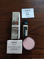 Photo showing all four cosmetics items together on a wooden surface: Marcelle BB Cream box, Maybelline Fit Me foundation bottle, NYX Bare With Me primer box, and CoverGirl Clean Fresh powder compact.
