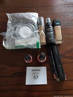 Photo showing all 9 cosmetics items laid out on a wooden surface including foundations, setting spray, nail polishes, lip liners, and makeup remover pads