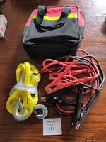 Car safety kit showing jumper cables, towing rope, and carrying bag on wooden surface.