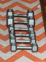 Three pairs of steel hex dumbbells arranged on an orange and white chevron-patterned surface next to a wooden furniture piece.