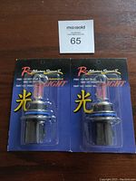Two new R-Motor Sports icy blue headlight bulbs in original packaging on a wooden surface with MaxSold lot number 65