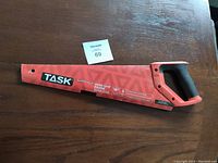 First image showing one TASK Super-Cut Hand Saw with blade cover and ergonomic handle placed on wooden surface with lot tag visible.