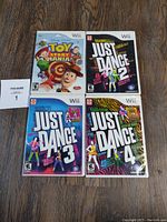 Four Nintendo Wii games arranged on a wooden floor: Toy Story Mania, Just Dance 2, 3, and 4 in original cases.