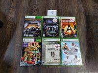 Six Xbox 360 game cases and discs arranged in two rows on a wood floor, titles clearly visible, sold as untested condition
