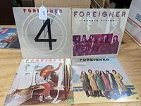 Four Foreigner LP albums upright showing front covers. Titles: 4, Double Vision, Head Games, Foreigner. Visible shelf wear and use signs.