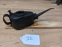 Side view of the antique Atkinson Haserick machine oiler showing handle, spout, and fill screw cap on wooden surface.