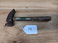 Antique cobbler's hammer showing the hammer claw head with wear and rust, wooden handle with paint remnants.