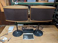 Front view of both speakers mounted on stands with equalizer unit and manual displayed on table.