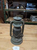 Front view showing green painted body, red glass globe, protective wire guard, and carrying handle