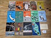 Group photo of 14 colorful General Motors booklets from the 1940s and 1950s arranged on a wooden surface.