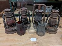 Four rusted metal lanterns with wire cages and three glass globes of different shapes and colors on table