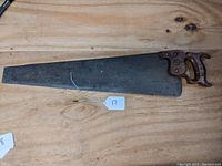 Full view of large vintage crosscut saw with wooden handle and steel blade showing aging and original etching traces.