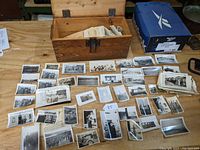 Wooden box open on table with numerous black-and-white photos and negatives spread out