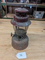 Full view of vintage lantern showing vented top cap, glass globe, metal frame and fuel reservoir with adjustment knob.