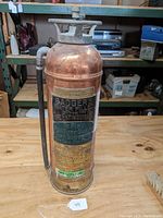 Full front view of the copper fire extinguisher sitting upright showing embossed and painted labels.