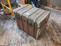 Side view of vintage bent wood steamer trunk showing metal straps, corner reinforcements, and general exterior condition.