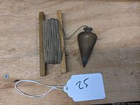 Photo of the plumb bob with the wooden reel and wound string beside it on a wooden surface.
