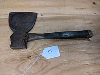 Front view of vintage hatchet showing the broad blade and wooden handle wrapped in black material, placed on wooden surface.