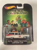 Front view of Hot Wheels Ecto-1 diecast car in original packaging, showing the detailed model and The Real Ghostbusters branding with character illustrations.