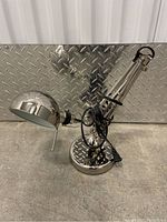 Full view of IKEA adjustable metal desk lamp with polished chrome finish showing articulated arm, round base, and lamp cord.