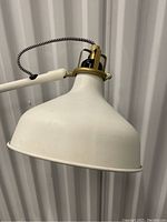 Close-up of white metal lamp shade with brass hardware and black and white braided cord