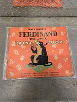 Front cover of the paint book showing Ferdinand the Bull in orange background with floral and butterfly motifs.