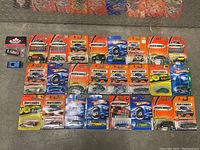 Full group photo showing 25 Matchbox and Hot Wheels die-cast cars in original packaging arranged on floor.