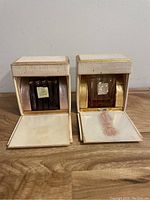 Two vintage perfume bottles displayed in open gold-tone cushioned boxes with satin lining and fabric wear.