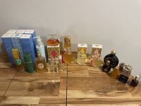 Full lot showing multiple vintage perfume bottles, boxes and lotion bottle arranged in two rows on wooden surface.