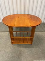 Full view of the wooden side table with the drop-leaf top extended and rotating design showing the magazine rack below.