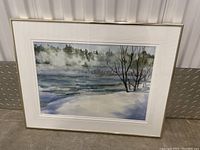 Framed watercolor painting depicting a winter river landscape with snowy riverbanks, bare trees, and misty background.