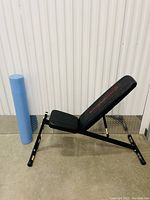 Adjustable black weight bench with padded seat and backrest against a white corrugated wall.