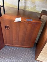 Closed view of wooden cabinet with circular recessed door handle, on a diamond plate floor against a yellowed wall.