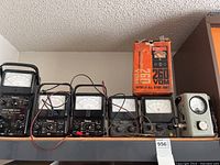 Shelf showing six black-cased analog meters and one gray vacuum tube voltmeter