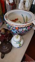 Photo of large ceramic pot with detailed floral exterior and fish painted inside, shown with other items for scale