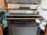 Stacked stereo and video equipment on shelf including a Sony DVD/VCD player on top, two Bang & Olufsen Beomaster audio units in the middle, and a Trinitron TV at bottom with remotes on top.