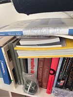 Image showing assortment of books on a shelf including a large blue hardcover world atlas, other hardcover books, and some paperbacks.