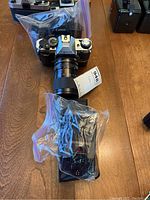 Front view of Canon AE-1 Program camera with attached zoom lens and wrapped flash unit in plastic bag on table.