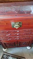 Close-up of the metal latch and floral carvings on the chest's drawers and front panel.