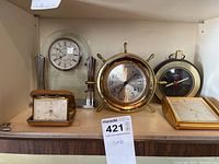 Five tabletop clocks displayed on a shelf, various styles and gold-tone finishes